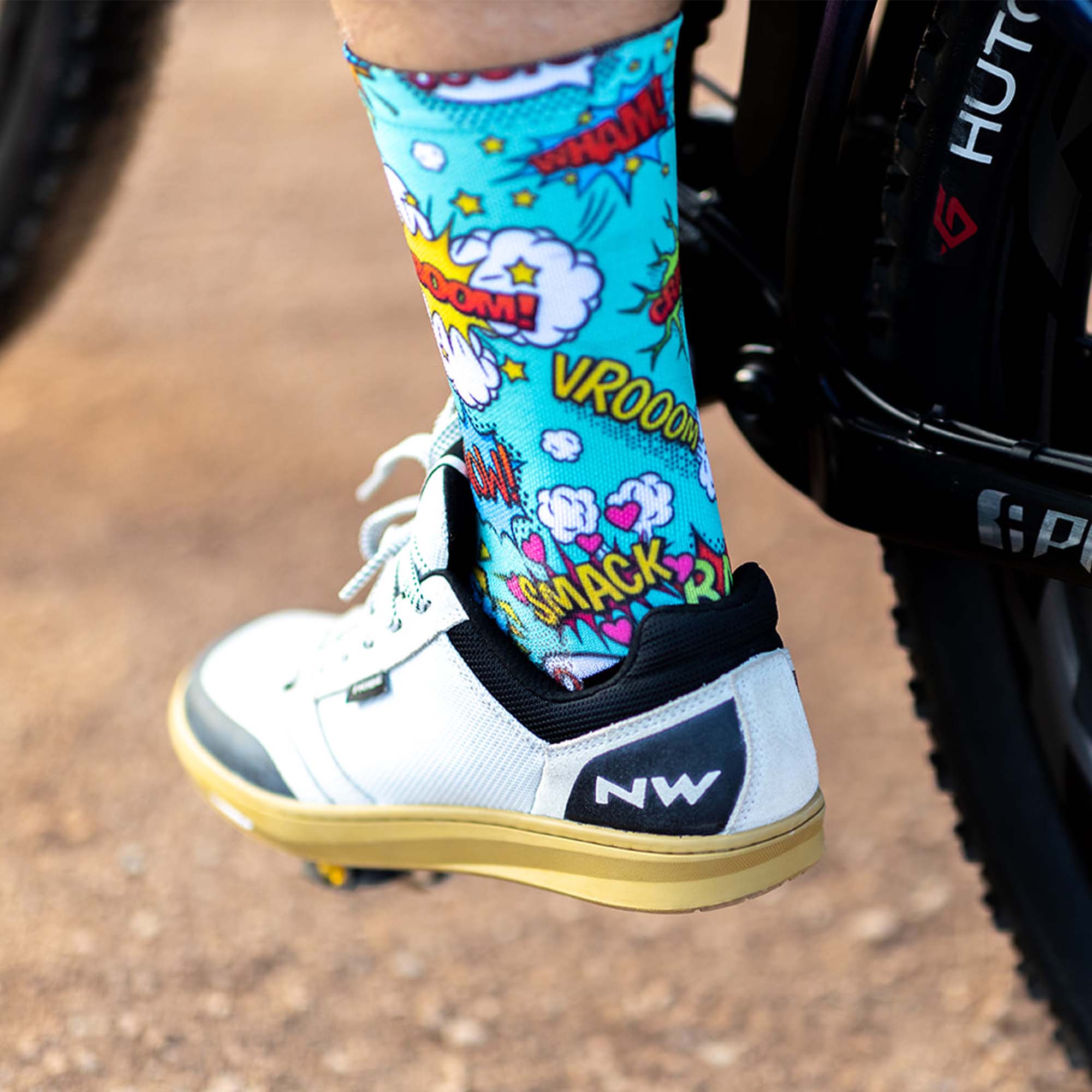Foot on bike pedal wearing white  flat sneaker and Sox Footwear Comic Socks