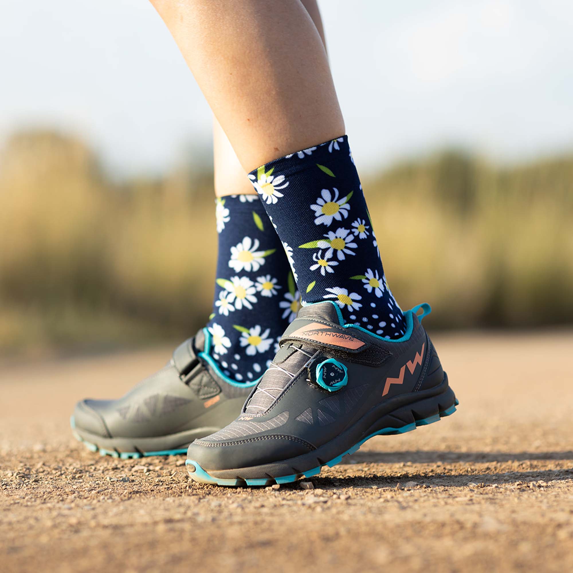 Girl wearing cycling shoes with Sox Footwear daisy sock design on them. The socks have a black background with white daisies on them.